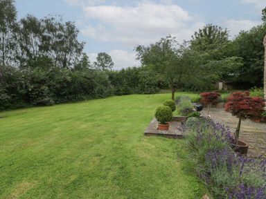 A garden with a lawn bushes trees potted plants and a stone patio at Owl Barn in Marston Stannett near Leominster