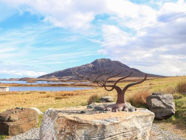 A metal sculpture resembling tree branches on a large rock with a mountain and lake in the background at North Light Studio Locheport near Lochmaddy North Uist