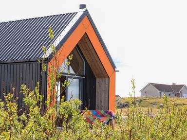 A black and orange house with a slanted roof and shrubs in front at North Light Studio in Locheport near Lochmaddy North Uist