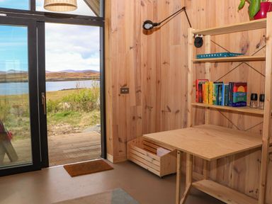 A wooden room with a desk bookshelf and large glass door overlooking a lake at North Light Studio in Locheport near Lochmaddy North Uist