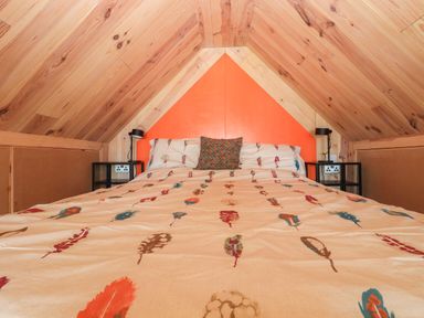 A bedroom with a bed and patterned bedding under a wooden sloped ceiling at North Light Studio in Locheport near Lochmaddy North Uist