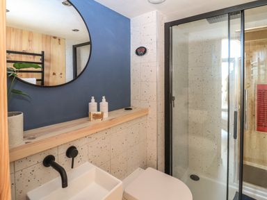 A bathroom with a round mirror above a sink with black fixtures and a glass shower enclosure at North Light Studio in Locheport near Lochmaddy North Uist