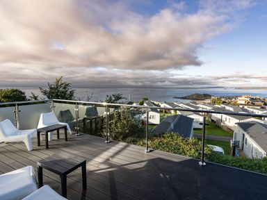 A balcony with white chairs and black tables overlooking cabins and the sea at Lanyon in St Ives