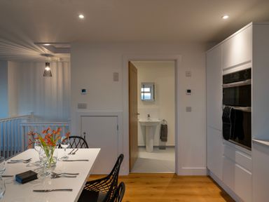 A kitchen dining area with a table set with glasses and cutlery a doorway leading to a bathroom with a sink and towel at Lanyon in St Ives