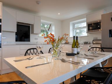 A kitchen with a white dining table set with wine glasses, cutlery, a vase with orange flowers, and two bottles of wine at Lanyon in St Ives