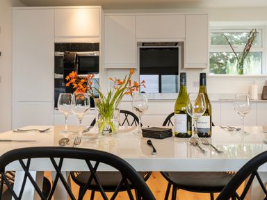 A dining table set with wine glasses cutlery bottles of wine and a vase of orange flowers in a kitchen at Lanyon in St Ives