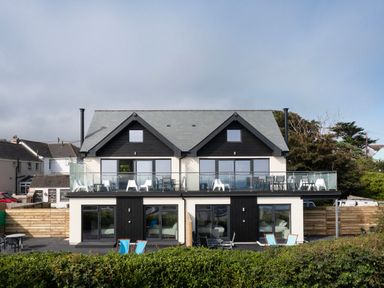 A two-story modern semi-detached house with balconies, patio furniture, and a hedge in front at Lanyon in St Ives