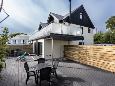 An outdoor patio area with tables and chairs next to a two-story house with a balcony at Lanyon in St Ives