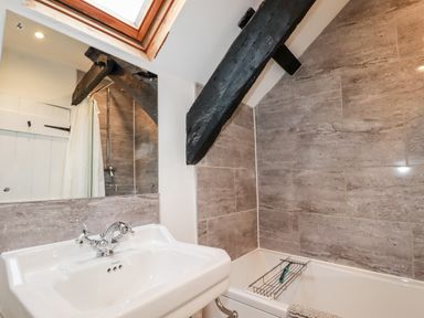 A bathroom with a sink a bathtub stone tile walls wooden ceiling beams and a skylight at Ivy Cottage Trenale near Tintagel
