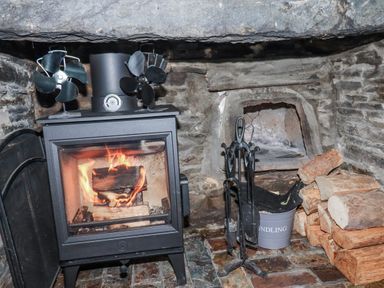 A wood stove with firewood and fans at Ivy Cottage in Trenale near Tintagel