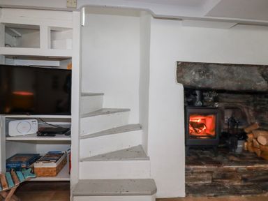 A living room with a staircase and a fireplace at Ivy Cottage in Trenale near Tintagel