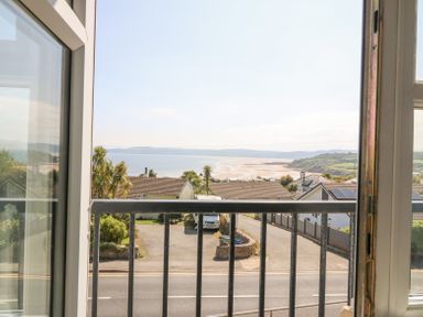 A view of a beach and houses from a window with a black balcony railing at Sea La Vie in Benllech