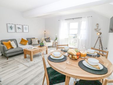 A living room and dining area with a gray sofa orange cushions wooden table and round dining table set with dishes at Sea La Vie in Benllech
