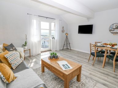 A living room with a sofa and coffee table and a dining table with chairs and a wall-mounted TV at Sea La Vie in Benllech