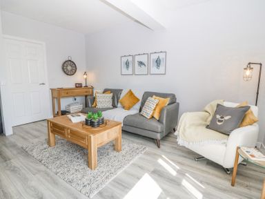 A living room with a gray sofa and white armchair wooden coffee table and console table with wall clock and framed pictures at Sea La Vie in Benllech