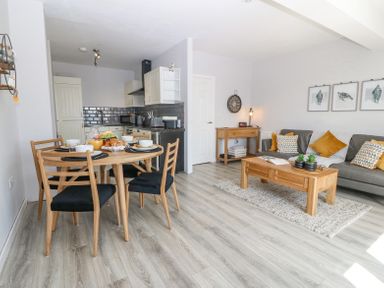 An open living area with a dining table and chairs kitchen cabinets a couch coffee table and wall art at Sea La Vie in Benllech