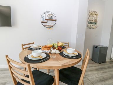 A dining area with a round wooden table set for four with bowls cups croissants fruit and orange juice at Sea La Vie in Benllech
