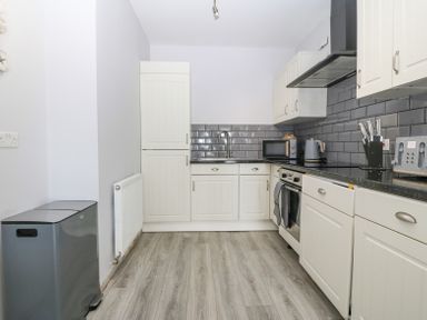 A kitchen with white cabinets gray subway tile backsplash and wood flooring at Sea La Vie in Benllech