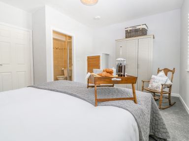 A bedroom with a bed with breakfast tray a wardrobe a rocking chair and an ensuite bathroom at Sea La Vie in Benllech