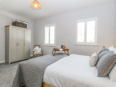 A bedroom with a bed with gray bedding cushions a wooden wardrobe and a chair with a cushion at Sea La Vie in Benllech