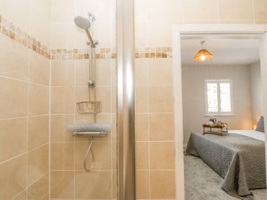 A shower area with beige tiles next to a bedroom with a bed and a tray on the bed at Sea La Vie in Benllech