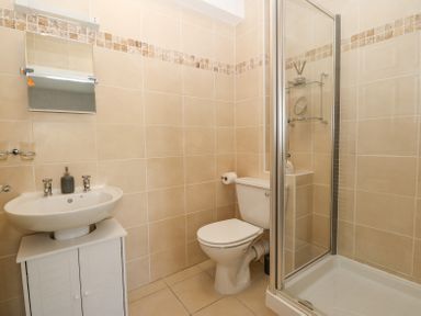 A bathroom with a sink on a cabinet a toilet and a corner shower enclosure at Sea La Vie in Benllech