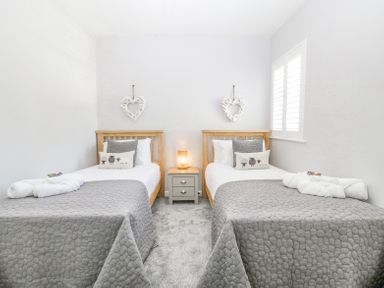 A bedroom with two single beds gray quilted bedspreads bedside table and lamp at Sea La Vie in Benllech