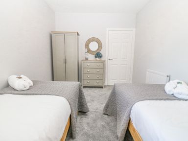 A bedroom with two single beds gray bedspreads a wardrobe and chest of drawers at Sea La Vie in Benllech
