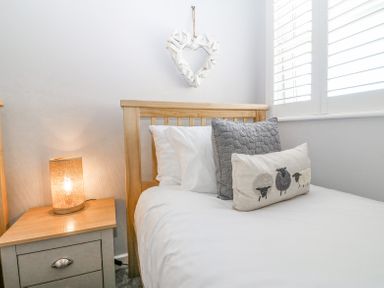 A bedroom with a wooden bed with pillows a bedside table with a lamp and a heart shaped decoration on the wall at Sea La Vie in Benllech