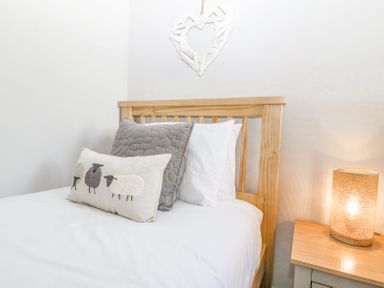 A bed with a wooden headboard and decorative pillows beside a wooden nightstand with a lit lamp at Sea La Vie in Benllech