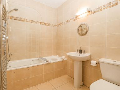 A bathroom with a bathtub shower combination a sink a toilet a towel rail and a round mirror at Sea La Vie in Benllech