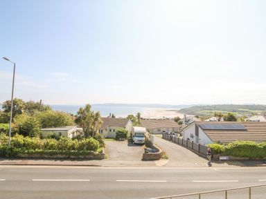 Houses and greenery near a road with a view of the beach and sea at Sea La Vie in Benllech