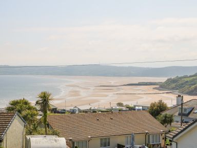 A coastal view with houses in the foreground palm trees and a sandy beach at Sea La Vie in Benllech