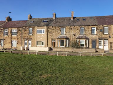 A row of stone terraced houses with front doors and windows facing a green lawn at Southview Amble in Amble