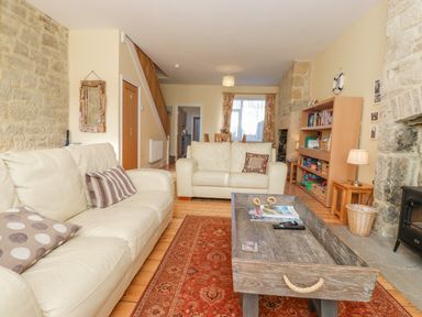 A living room with two cream sofas a wooden coffee table a red patterned rug a wooden bookshelf and a stone fireplace at Southview Amble in Amble