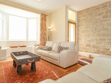 A living room with white sofas a stone wall a wooden coffee table and a bay window with cushions at Southview Amble in Amble