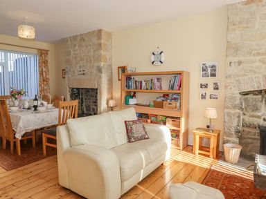 A living room with a white sofa, bookshelf, dining table with chairs, and stone fireplace at Southview Amble in Amble