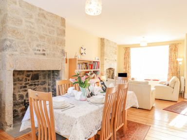 A dining and living room with a stone fireplace wooden chairs a dining table with flowers and a bookshelf at Southview Amble in Amble