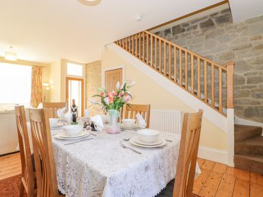A dining room with a wooden table set with bowls plates and glasses in front of a staircase at Southview Amble in Amble