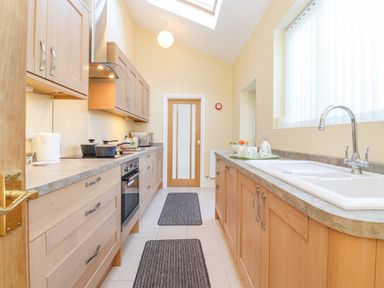 A narrow kitchen with wooden cabinets a sink a stovetop an oven a microwave and ceiling skylight at Southview Amble in Amble