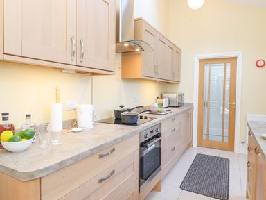 A kitchen with wooden cabinets a built-in oven a stovetop pots a microwave a kettle a bowl of fruit and a striped rug on the floor at Southview Amble in Amble