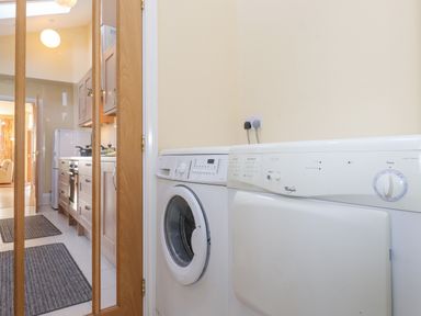 A laundry area with a washing machine and dryer next to a kitchen with wooden cabinets and a refrigerator at Southview Amble in Amble