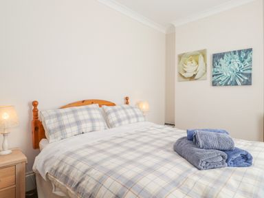 A bedroom with a wooden bed with plaid bedding folded towels on the bed bedside tables with lamps and floral wall art at Southview Amble in Amble