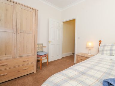 A bedroom with a wooden wardrobe chair bedside table with lamp and a bed with checkered bedding at Southview Amble in Amble