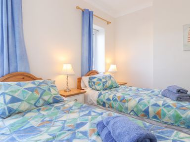 A bedroom with two single beds with patterned bedding blue curtains and bedside lamps at Southview Amble in Amble