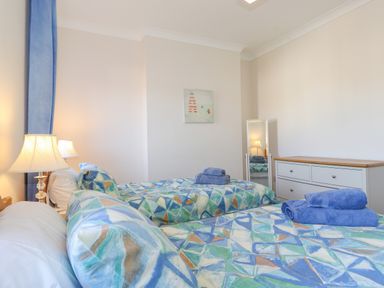 A bedroom with two single beds with geometric patterned bedding blue towels on beds a dresser a standing mirror and two lamps at Southview Amble in Amble