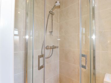A shower area with glass doors and a wall-mounted showerhead in a tiled bathroom at Southview Amble in Amble