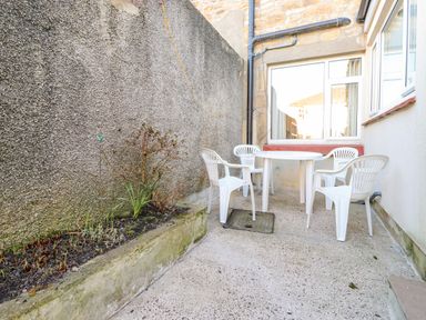 An outdoor patio area with a round table and four plastic chairs beside a raised planter with plants at Southview Amble in Amble