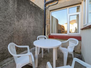 An outdoor patio area with a round white plastic table and four white plastic chairs next to a window at Southview Amble in Amble