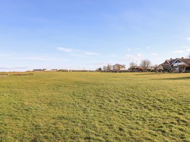An open grassy field with houses and trees in the background at Southview Amble in Amble